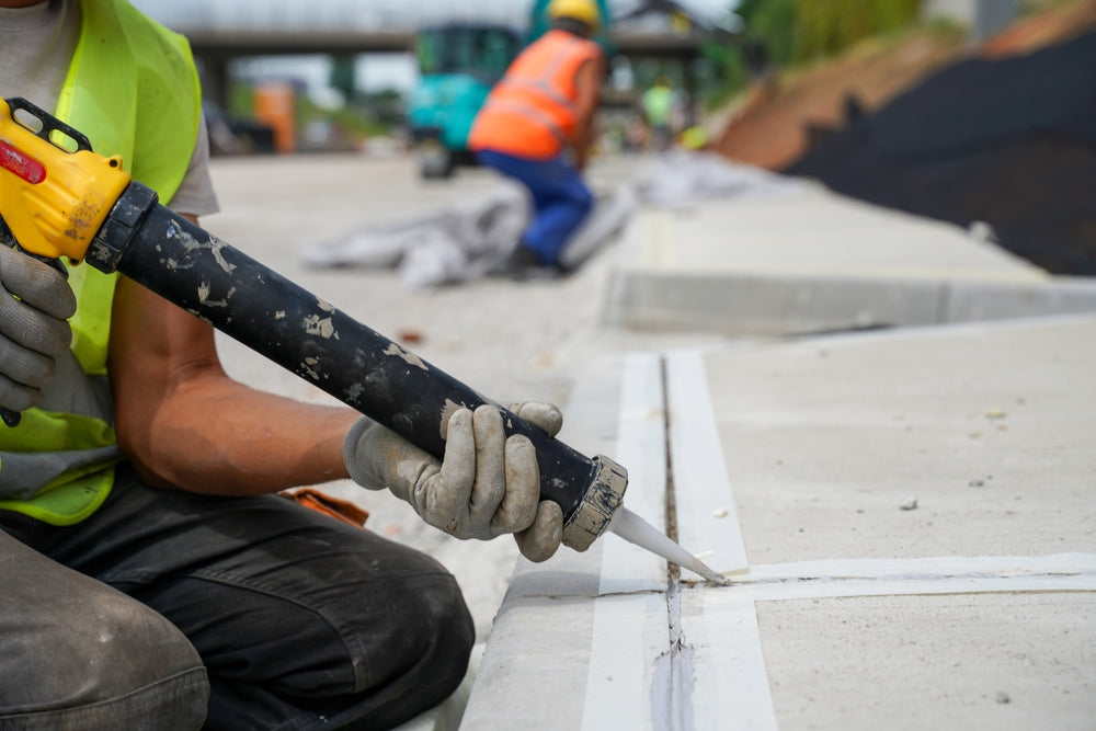Contractor applying sealant to a concrete expansion joint during construction.