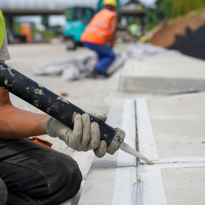 Contractor applying sealant to a concrete expansion joint during construction.