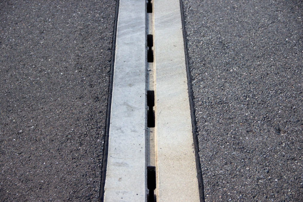 Concrete expansion joint is visible in asphalt pavement, highlighting the gap for movement, surrounded by textured black asphalt, illustrating engineering principles
