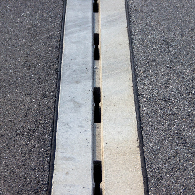 Concrete expansion joint is visible in asphalt pavement, highlighting the gap for movement, surrounded by textured black asphalt, illustrating engineering principles