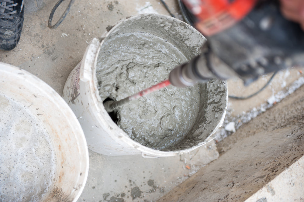 Mixing concrete with a handheld concrete mixer.