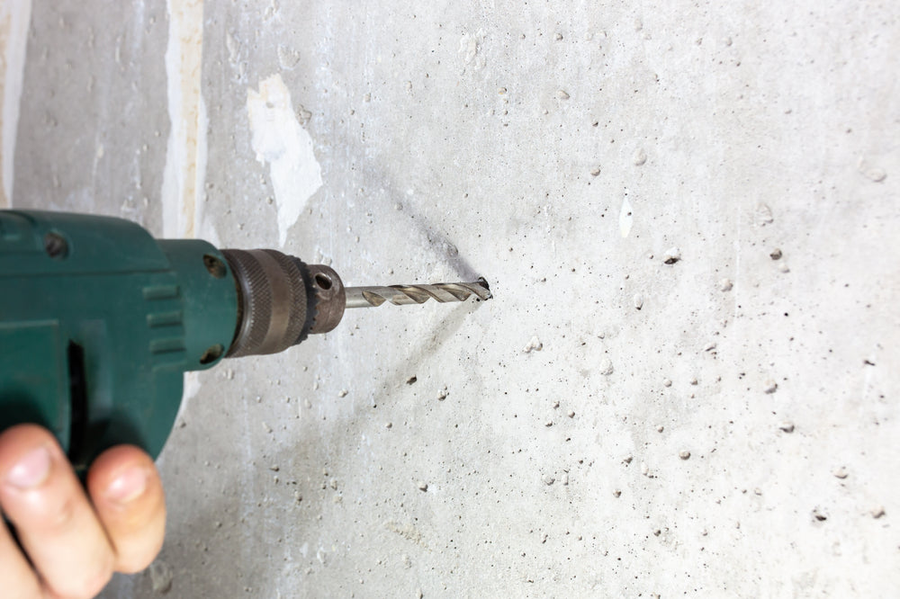 Man is drilling hole in the concrete wall. Proper drill bit for drilling concrete. 