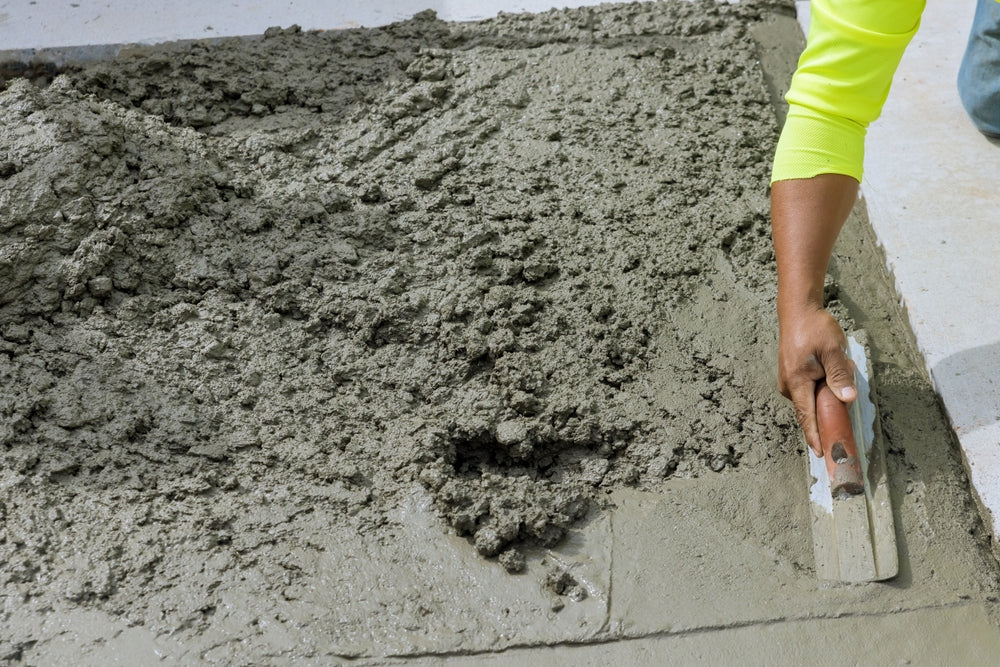 On freshly poured concrete sidewalk worker holds steel trowel in process of smoothing it leveling