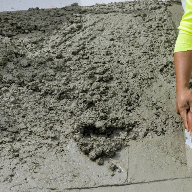 On freshly poured concrete sidewalk worker holds steel trowel in process of smoothing it leveling